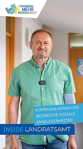 Mann in grünem Hemd mit Gerät am Brusttaschenbereich und Verband am rechten Arm steht in einem Flur mit Holztüren.